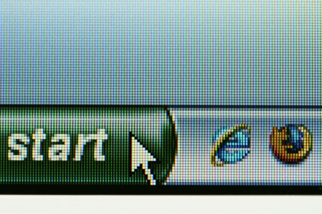 Close-up of a computer screen displaying the lower-left corner of a Windows interface with the classic green "Start" button. A cursor hovers over it, and two browser icons, Internet Explorer and Firefox, are visible in the taskbar.