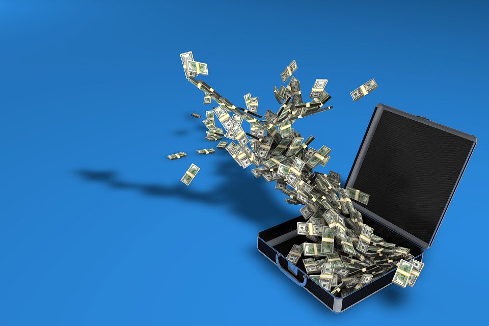 An open briefcase on a blue background with numerous U.S. dollar bills dramatically flying out, creating a swirling pattern.
