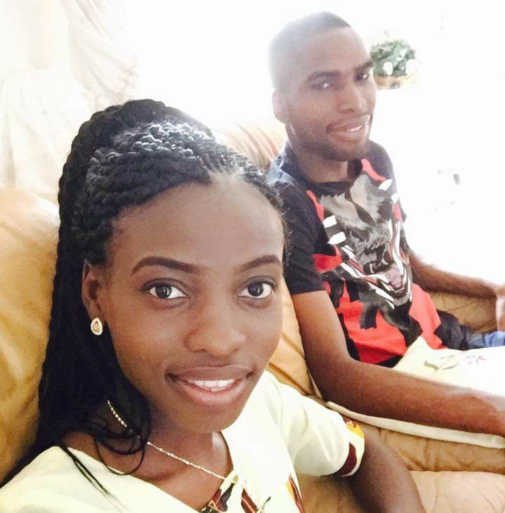 A woman and a man are sitting on a couch, smiling at the camera. The woman has braided hair and is wearing a light-colored top. The man is wearing a graphic t-shirt. They appear to be in a brightly lit room.