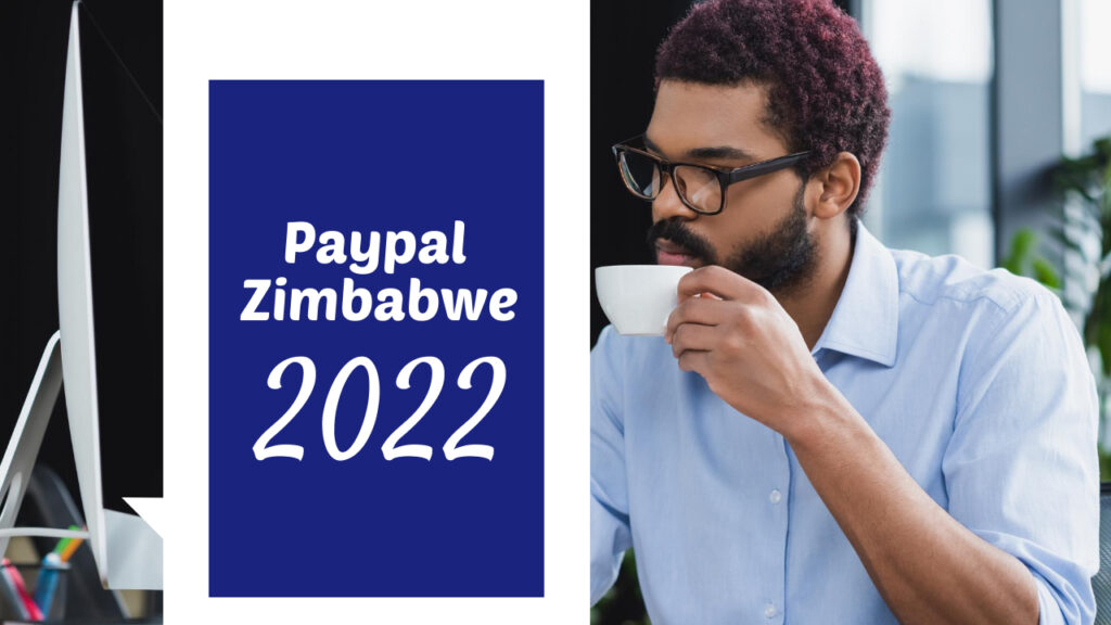A person wearing glasses is sipping from a cup while looking at a computer monitor. A large blue and white banner next to them reads "Paypal Zimbabwe 2022.